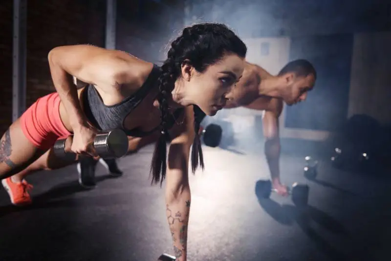 A couple performing dumbell push ups for five reps, trying to secure a set of new gym PRs.