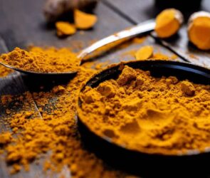 A bowl of turmeric powder next to a spoon, ready to be used as part of a balanced diet for weight loss.
