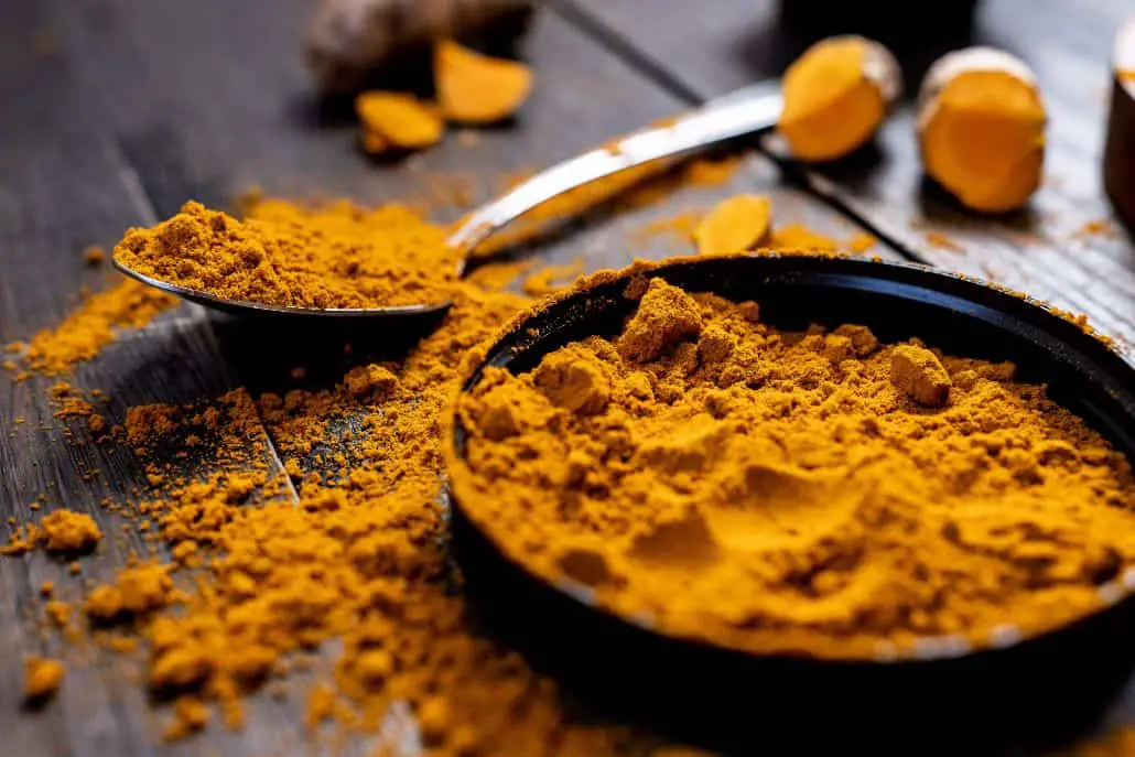 A bowl of turmeric powder next to a spoon, ready to be used as part of a balanced diet for weight loss.