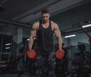 A muscular man holding a pair of red dumbells.